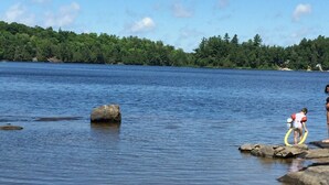 A lake with clear water, a sandy shore, and a person standing on rocks. - West Facing Private Cottage Oasis On Beautiful Isabella Lake Near Parry Sound (Parry Sound)