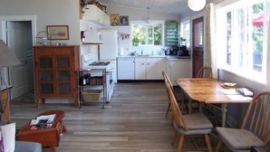 A spacious kitchen with white cabinets, a wooden dining table, and a view of the outdoors through large windows. - Private waterfront cottage on Malaspina Strait with easy access to town/trails (Powell River)