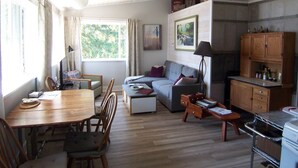 A cozy living room with a wooden dining table, a sofa, and a kitchen area with wooden cabinets. - Private waterfront cottage on Malaspina Strait with easy access to town/trails (Powell River)