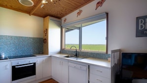 A kitchen with white cabinets, a tiled backsplash, a window with a view of the countryside, and a built-in oven. - Far View - Pets,  Linen,  Wi-Fi, Netflix, Caravan, EV charger (Venus Bay)