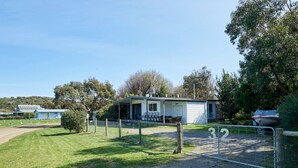 A small, single-story building with a covered porch and a fenced area. - Far View - Pets,  Linen,  Wi-Fi, Netflix, Caravan, EV charger (Venus Bay)