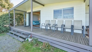 A modern house with a covered porch, a seating area with chairs, and a visible interior with a sofa and a window. - Far View - Pets,  Linen,  Wi-Fi, Netflix, Caravan, EV charger (Venus Bay)