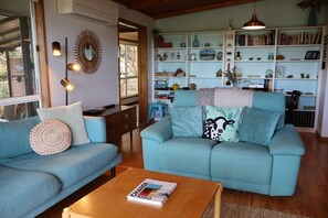 A living room with two sofas, a coffee table, and a bookshelf filled with books and decorative items. - Far View - Pets, Linen, Wi-Fi, Netflix, Free EV charger (Venus Bay)