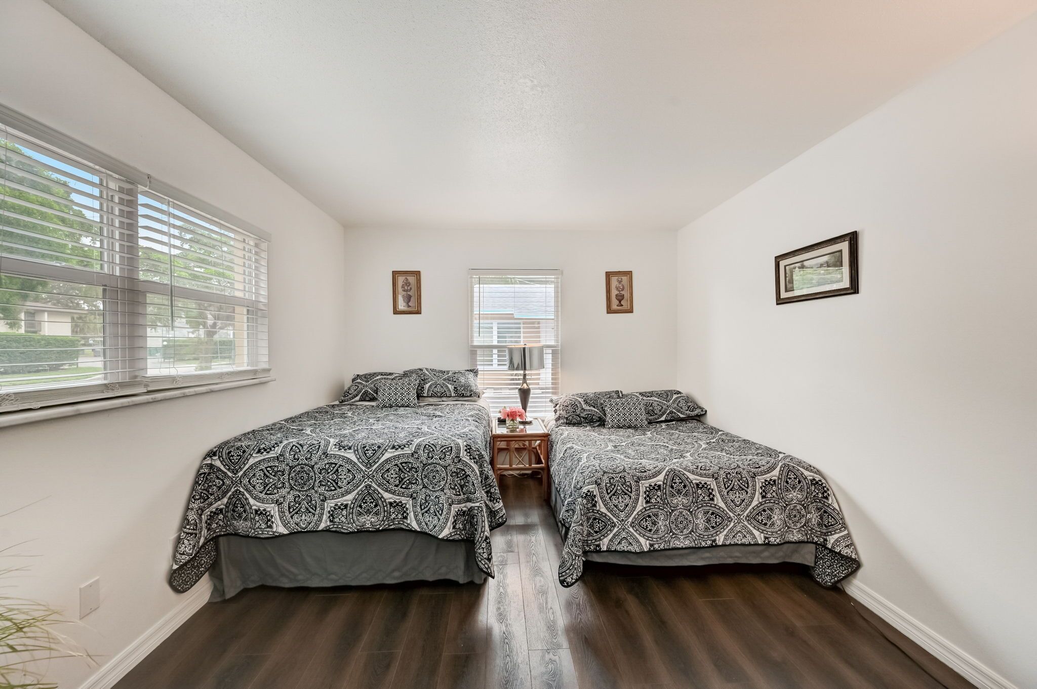 A bedroom with two beds, a small table, and a window with blinds.