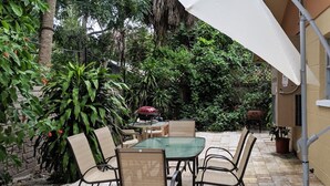 An outdoor patio with a table and chairs, surrounded by lush greenery and a white umbrella. - Sarasota Downtown Apartment!!! (Sarasota)