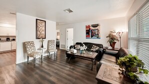 A modern living room with a dark wood floor, a leather sofa, a coffee table, and a dining area with a kitchen in the background. - Sarasota Downtown Apartment!!! (Sarasota)