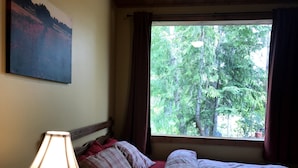 A bedroom with a bed, a lamp, a window with curtains, and a painting on the wall.
