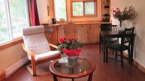 A cozy cabin interior with a wooden chair, a dining table with chairs, a kitchen area, and a large window.