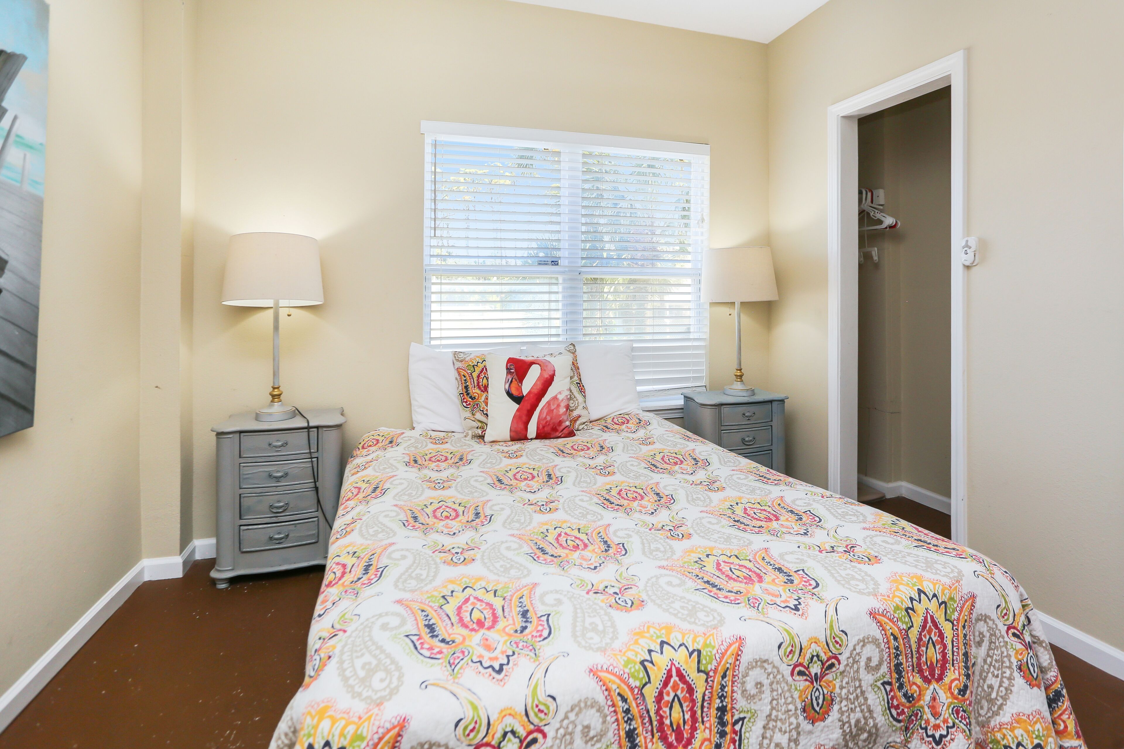 A bedroom with a bed, two nightstands, a window with blinds, and a door.