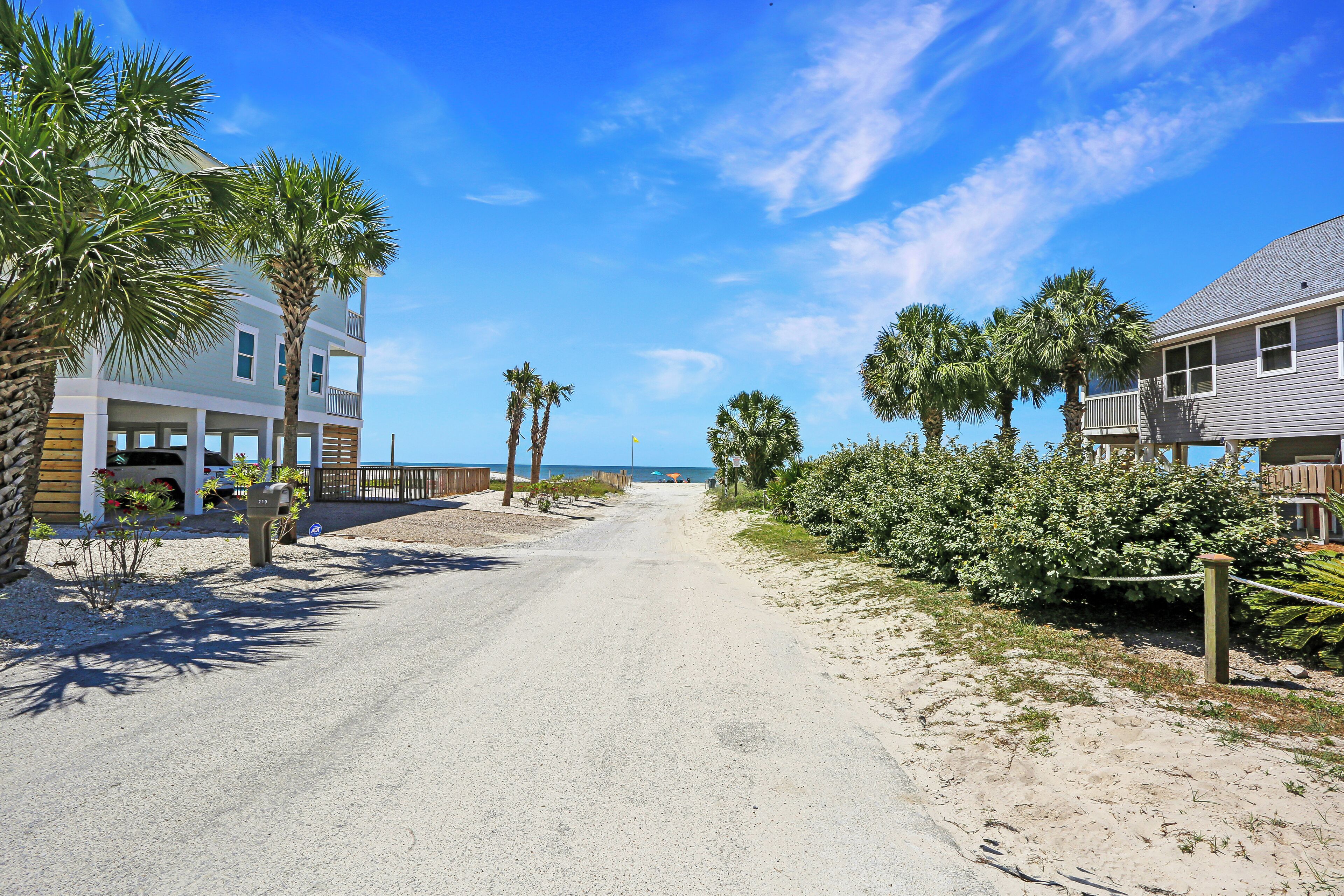 A coastal road with houses on both sides, palm trees, and a clear blue sky.