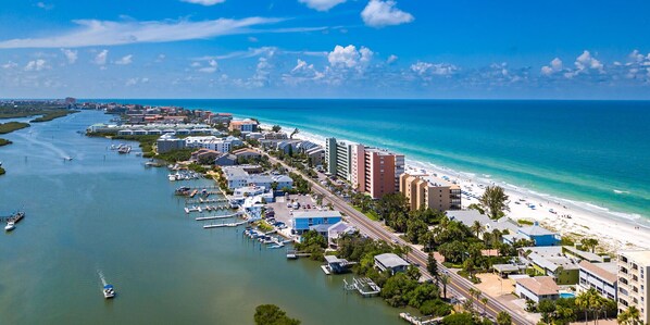 An aerial view of a coastal city with a marina, beachfront hotels, and a clear blue sky.
