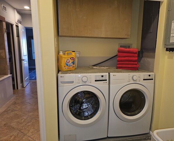 A laundry area with two LG front-loading washing machines, a yellow detergent container, and red towels stacked on top. - Waterfront Luxury Oasis - Steps to Beach
- Kayaks, Private Dock & Patio π (Indian Rocks Beach)