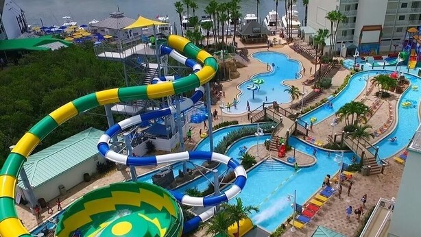 Un parc aquatique doté de nombreux toboggans et de plusieurs piscines, entouré de palmiers et comprenant une zone de plage.