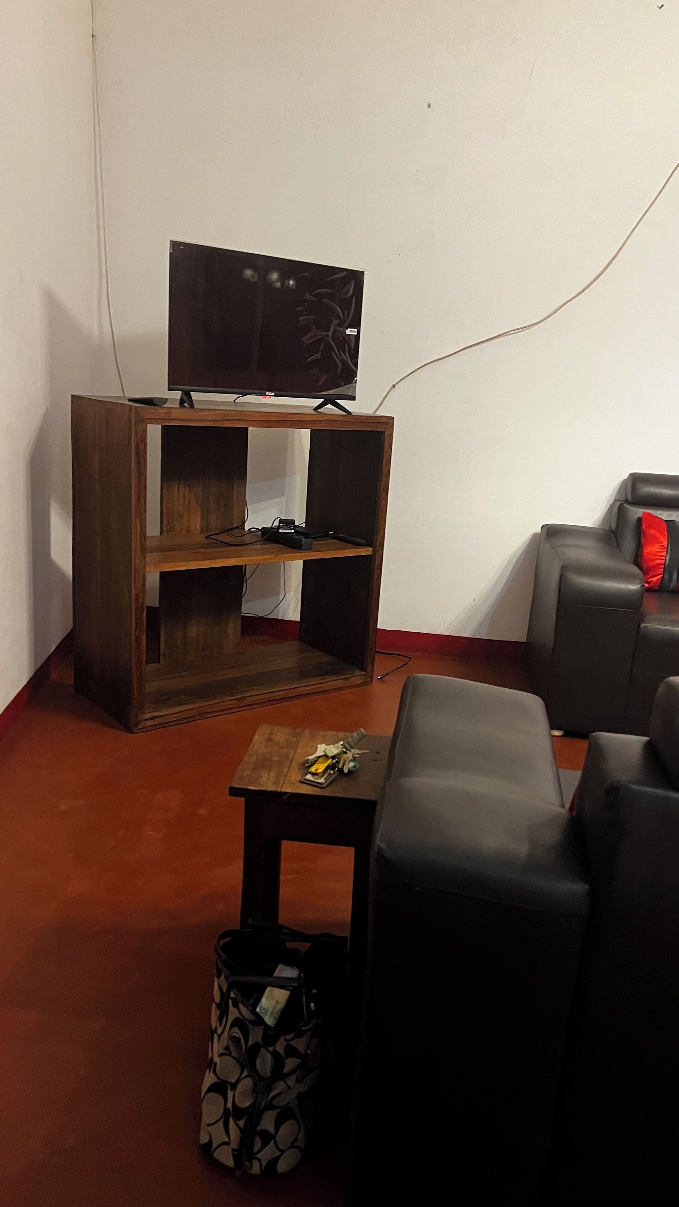 Ein Wohnzimmer mit einer Holzunterhaltungsecke, einem Fernseher, einem kleinen Tisch, einer gemusterten Tasche und schwarzen Ledersofas.