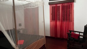 A bedroom with a four-poster bed, a nightstand, a lamp, and a chair.