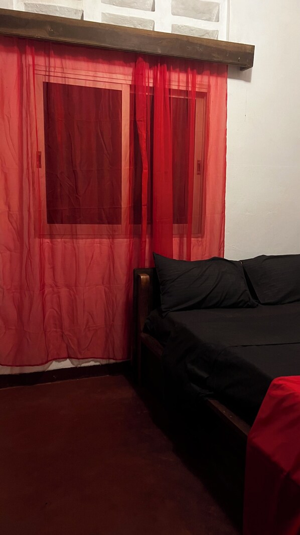 A room with a bed, a window with red curtains, and a wooden headboard.