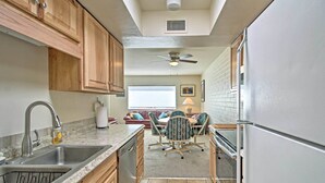A compact kitchen with wooden cabinets, a built-in dishwasher, a sink, and a dining area with a table and chairs. - Green Valley Townhome w/ Patio & Resort Amenities (Green Valley)