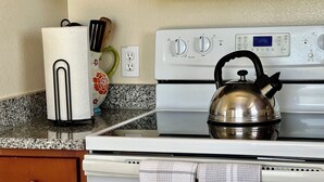 A kitchen with a stove, kettle, and a roll of paper towels.