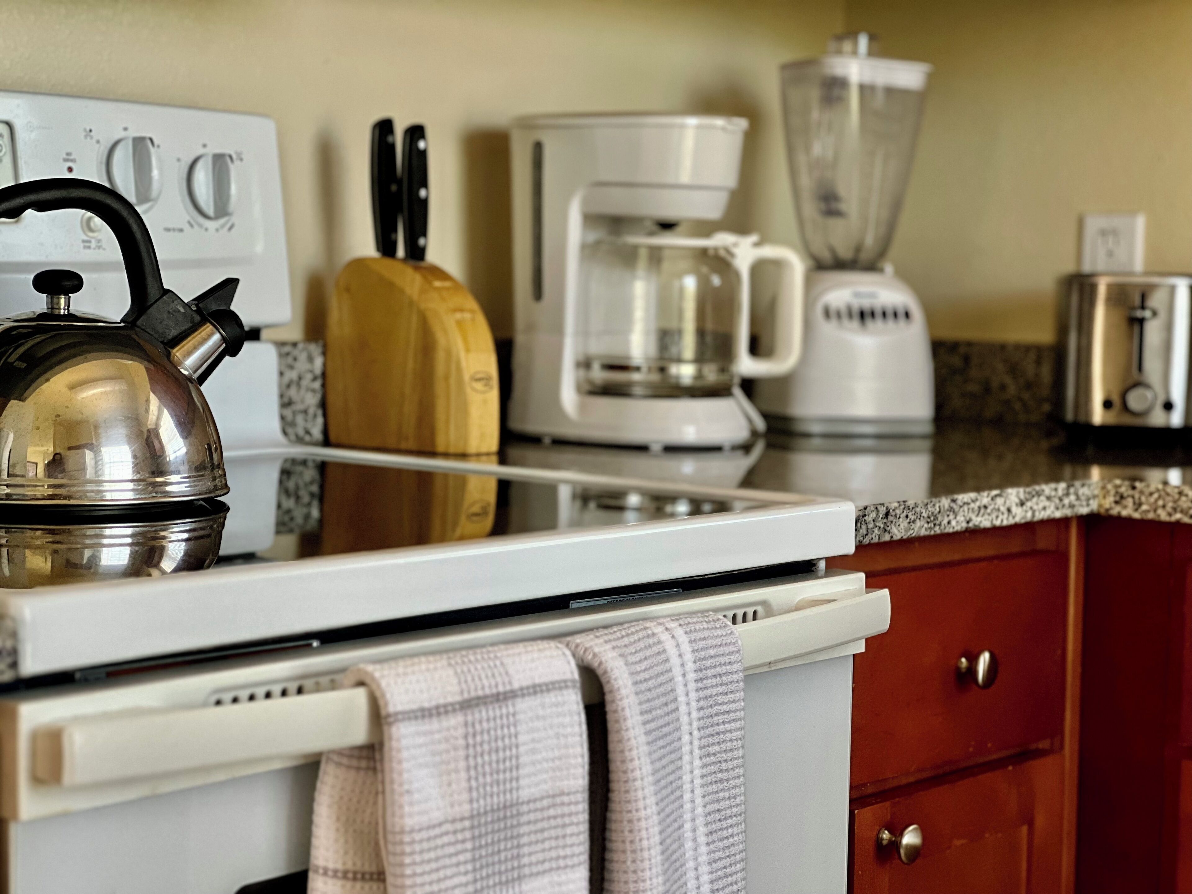 Una cocina con tetera, cafetera, licuadora, tostadora y tabla de cortar de madera.
