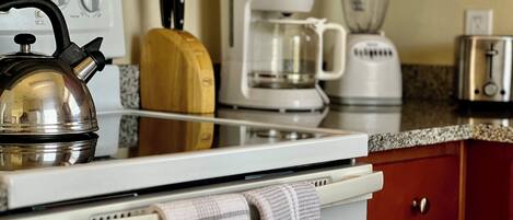 Una cocina con tetera, cafetera, licuadora, tostadora y tabla de cortar de madera.