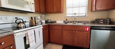 Una cocina con armarios de madera, una estufa blanca, microondas, fregadero y lavavajillas.