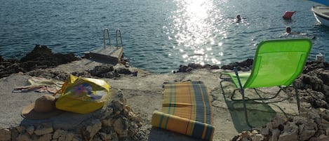 A beach with a pool, lounge chairs, and a towel on the sand.