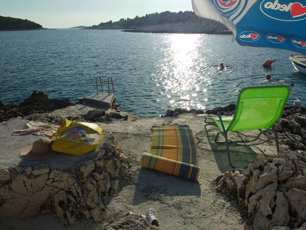A beach with a pool, lounge chairs, and a towel on the sand.