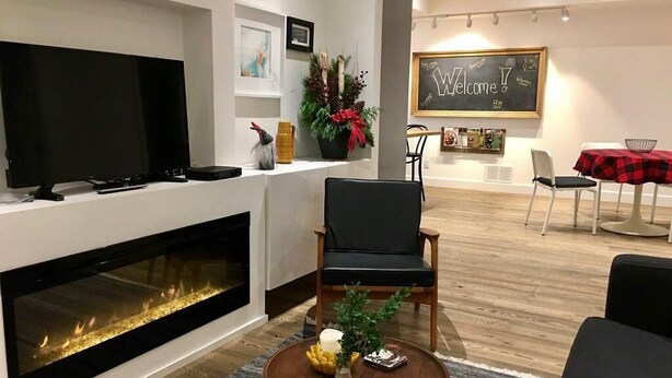Een moderne woonkamer met een open haard, een televisie, een comfortabele fauteuil en een bijzettafeltje met een vaas en kaarsen.