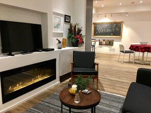 A modern living room with a fireplace, a television, a comfortable chair, and a small table with a vase and candles. - Delair park, free parking , long-term, pets ok (Abbotsford)