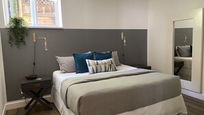 Een slaapkamer met een bed, nachtkastjes, een hangplant en een raam.