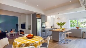Een moderne keuken met een centraal eiland, inbouwapparatuur en een eethoek met een geruit tafelkleed.