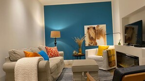 Een woonkamer met een blauwe accentmuur, een zithoek, een salontafel, een televisie en een open haard.