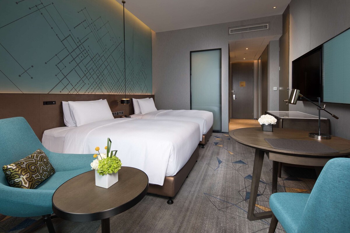 A hotel room with a large bed, two bedside tables, a desk with a chair, a TV, and a decorative wall piece.