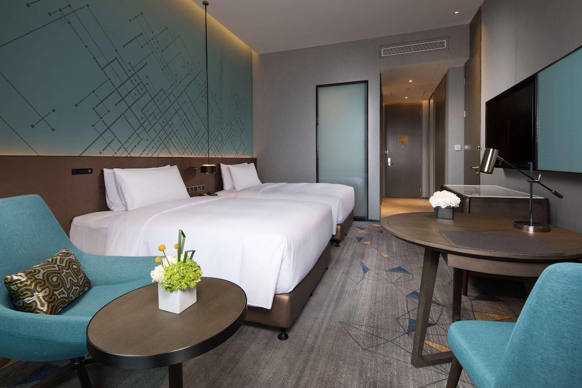 Ein Hotelzimmer mit einem großen Bett, zwei Nachttischen, einem Schreibtisch mit Stuhl, einem Fernseher und einer Wanddekoration.