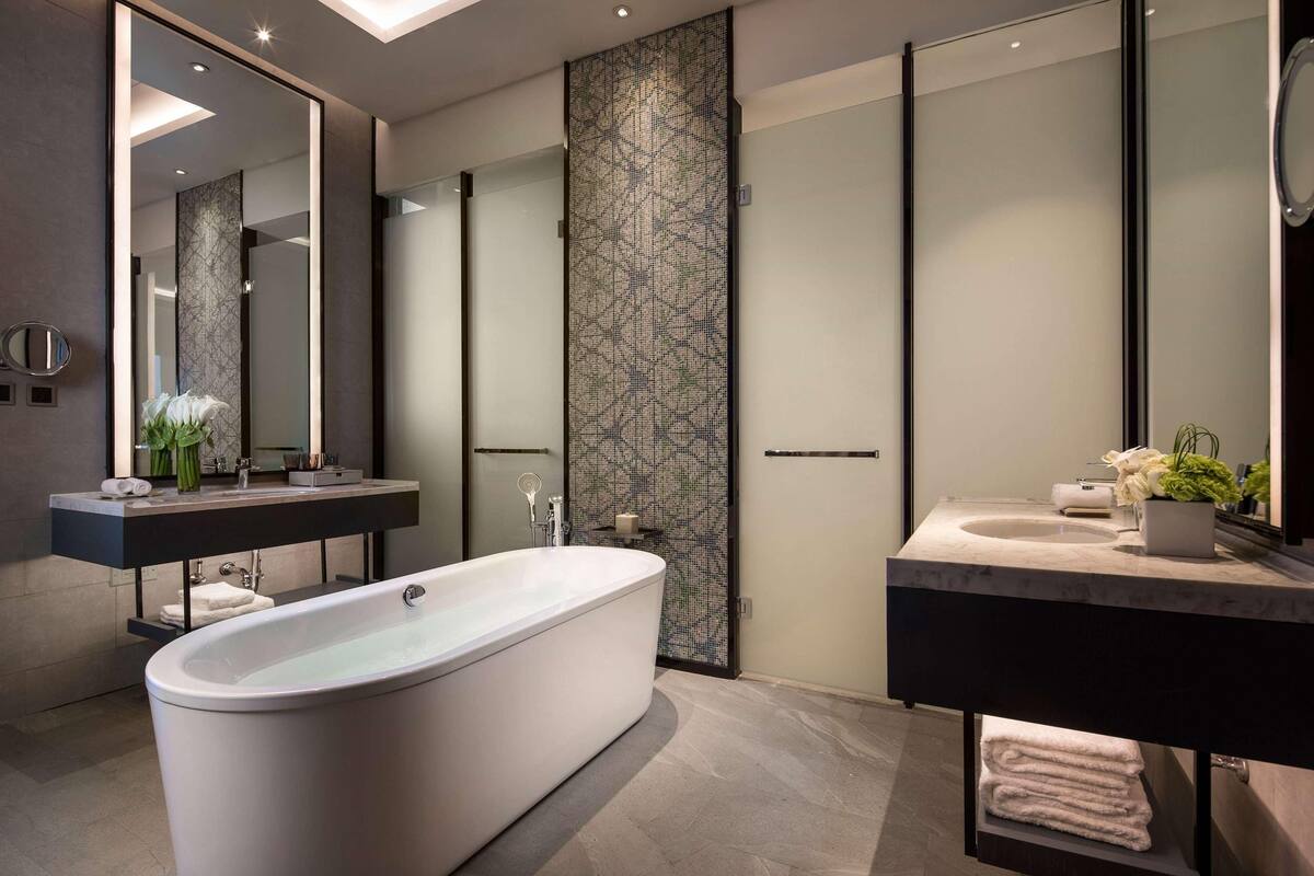 Ein modernes Badezimmer mit einer freistehenden Badewanne, einem Waschtisch mit Spiegel und einer dekorativen Wandverkleidung.