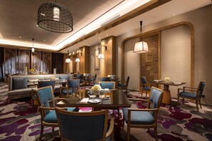 A hotel dining area with a round table, chairs, and a sofa. - Doubletree by Hilton Qingdao Oriental Movie Metrop (Qingdao)