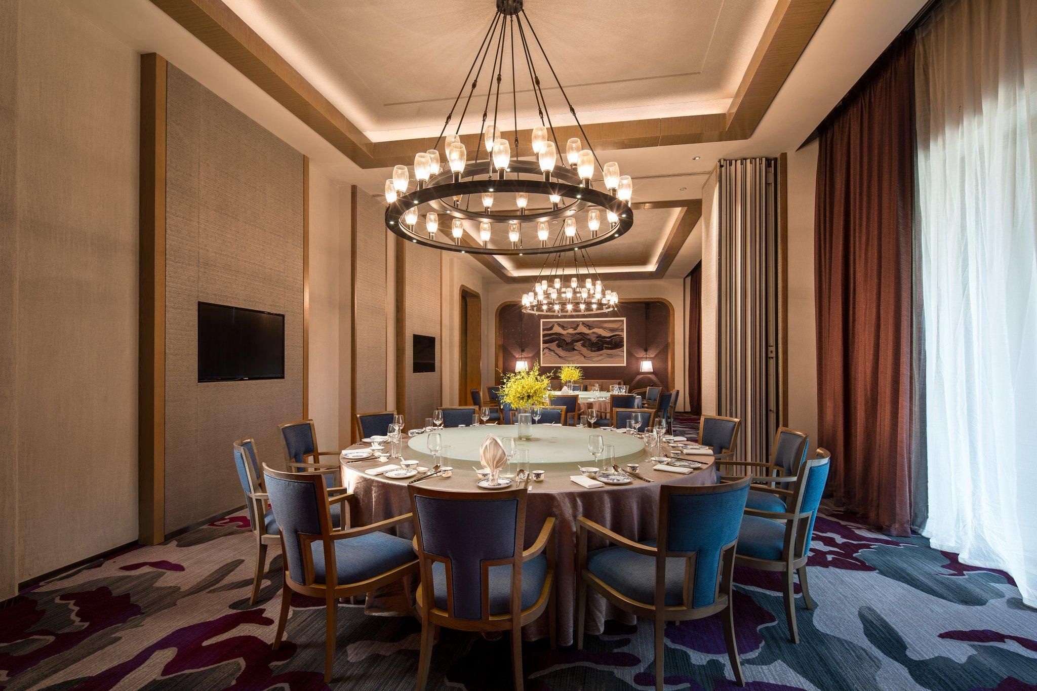 A conference room with a round table, blue chairs, a chandelier, and a large painting on the wall.