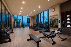 A gym with exercise equipment, large windows, and a clock on the wall. - Doubletree by Hilton Qingdao Oriental Movie Metrop (Qingdao)