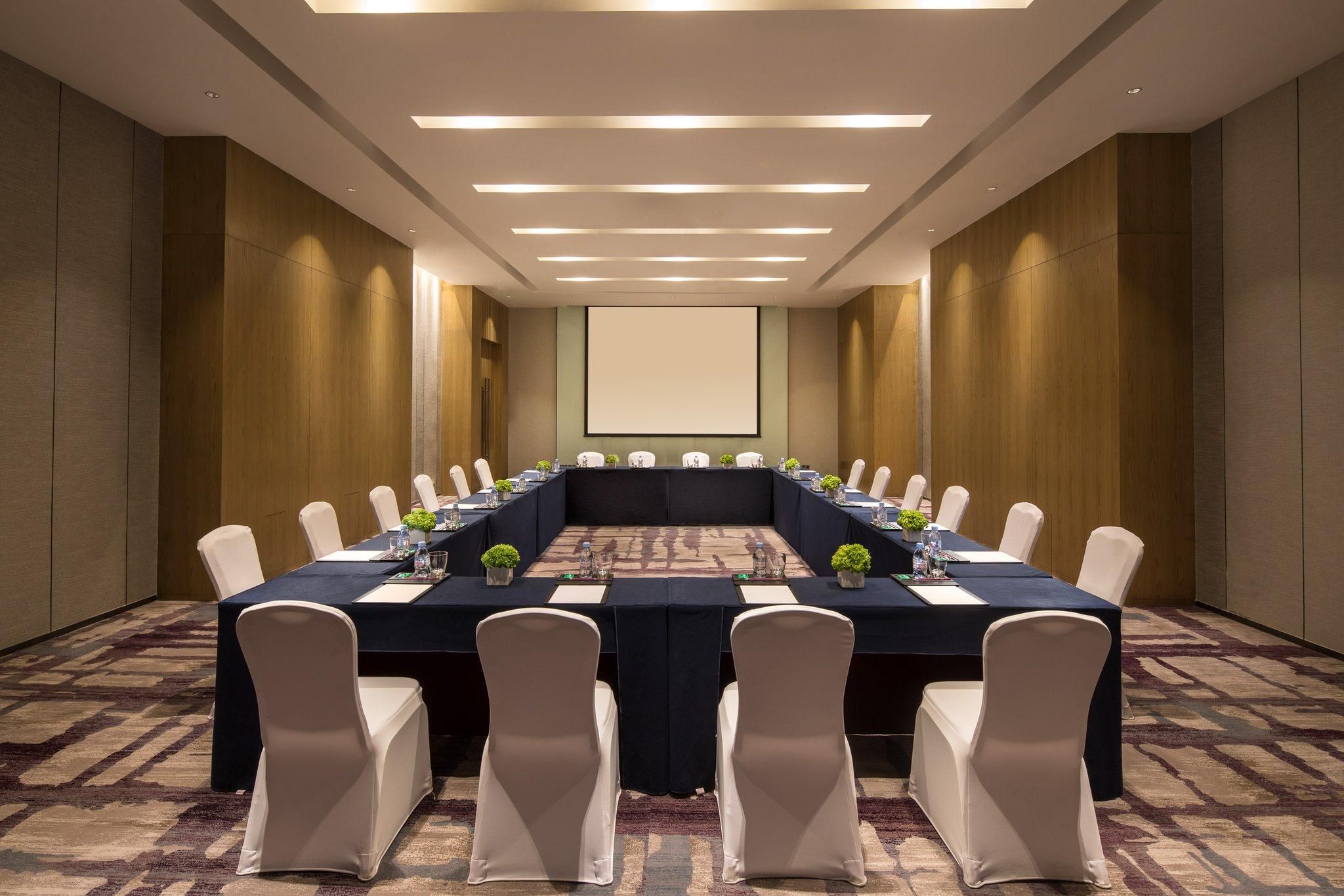 A conference room with a long table, white chairs, and a projector screen.