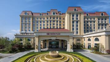 A large hotel with a central entrance, a fountain in front, and a clear sky.