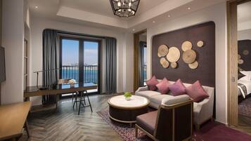A modern hotel room with a balcony, a sofa set, a dining table, and a large window with curtains.