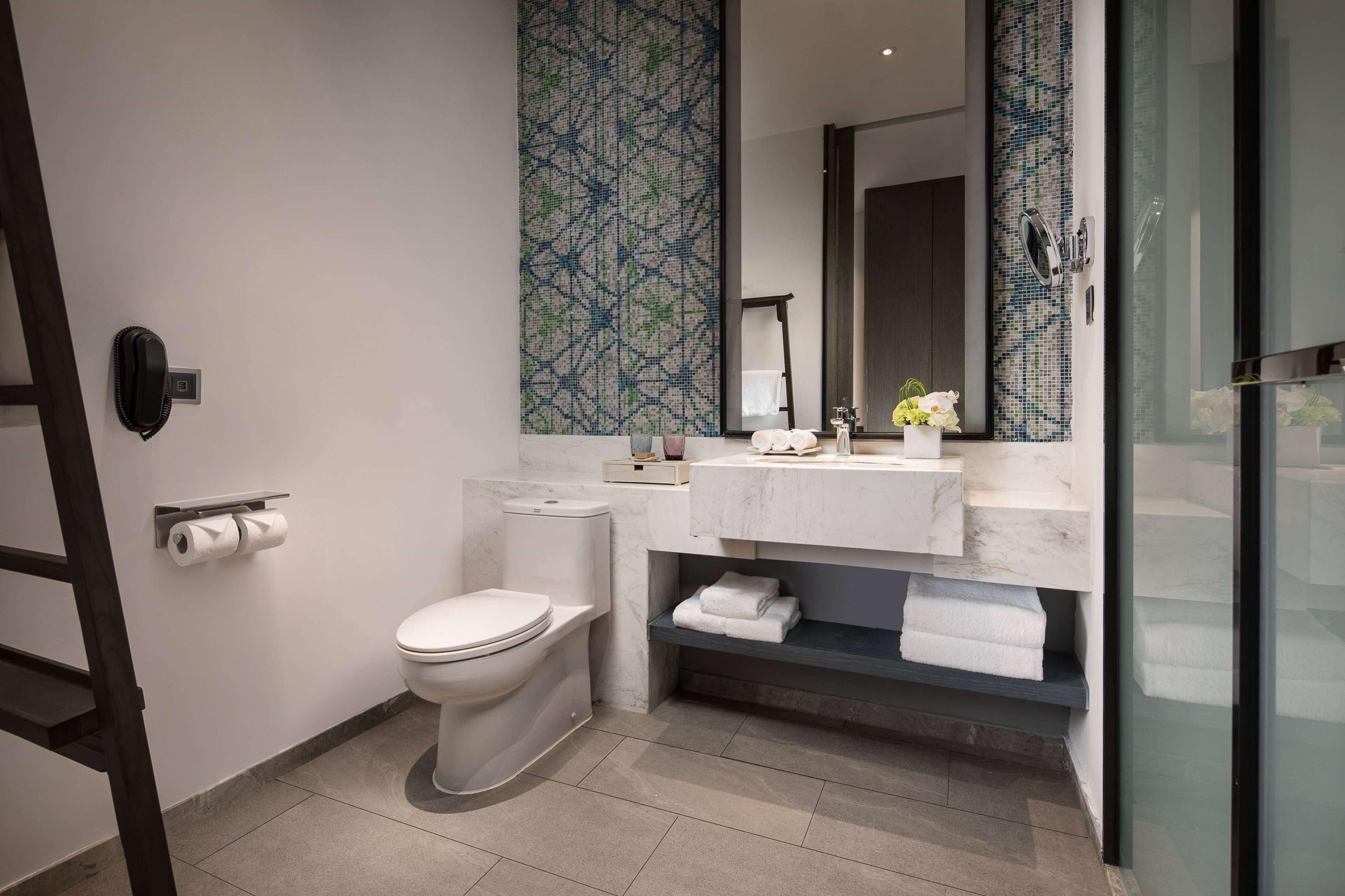 A modern bathroom with a toilet, a sink with a marble countertop, a mirror, and a glass shower enclosure.