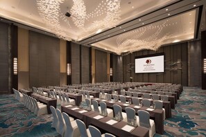 A conference room with rows of tables and chairs, a large screen displaying the DoubleTree logo, and a ceiling with a unique light fixture. - Doubletree by Hilton Qingdao Oriental Movie Metrop (Qingdao)