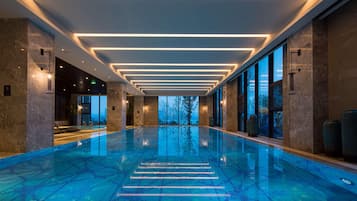 A modern indoor swimming pool with a clear view of the sky through large windows.
