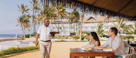 A resort patio with a thatched roof, a pool, and palm trees.