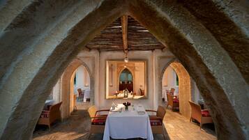 An arched dining area with a table set for two, flanked by wicker chairs, under a wooden ceiling.