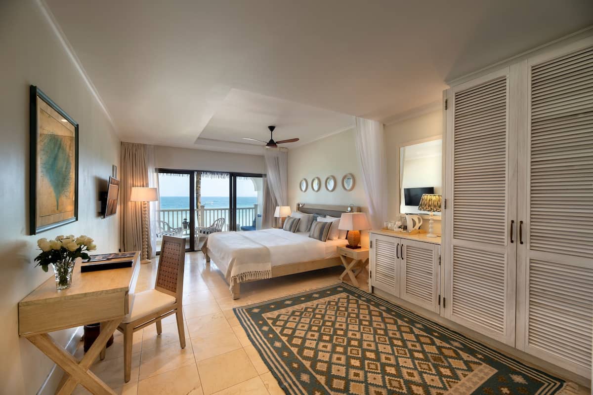 Habitación de hotel con cama, escritorio con silla, mesa de comedor, balcón con vistas y armario.