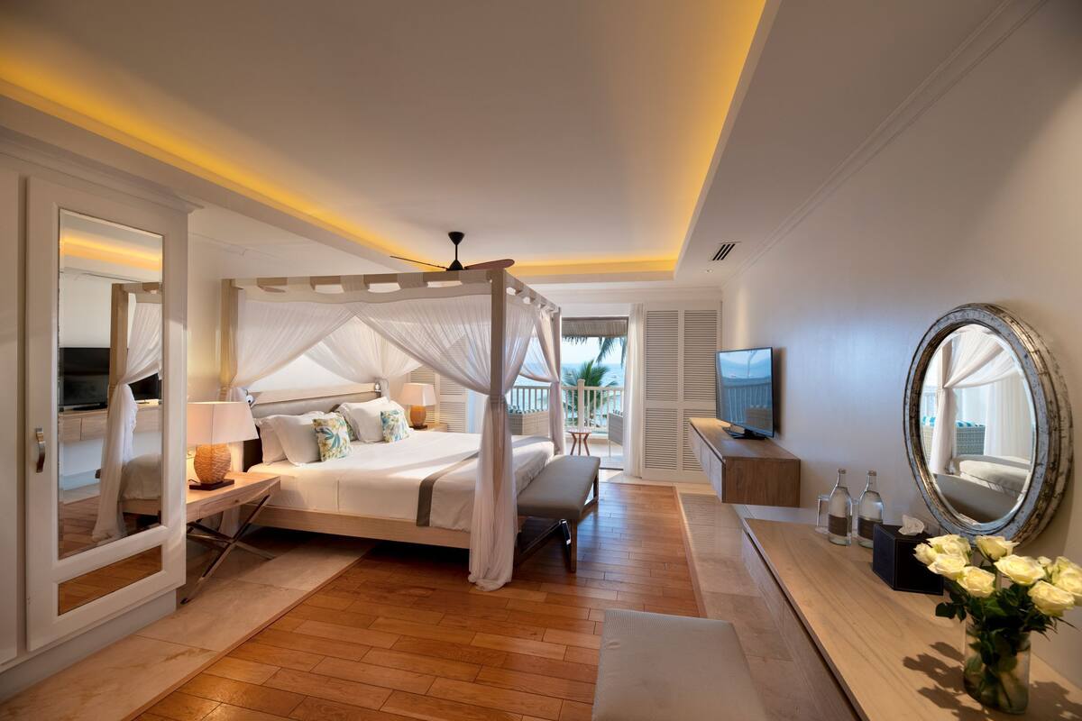 Un dormitorio con cama con dosel, televisión, espejo grande y vistas al exterior.