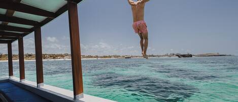 A man jumping off a boat into turquoise water with a beach and palm trees in the background.