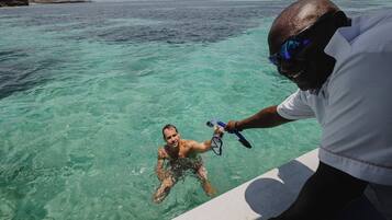 Una persona en aguas cristalinas, posiblemente haciendo snorkel, mientras otra persona ayuda.